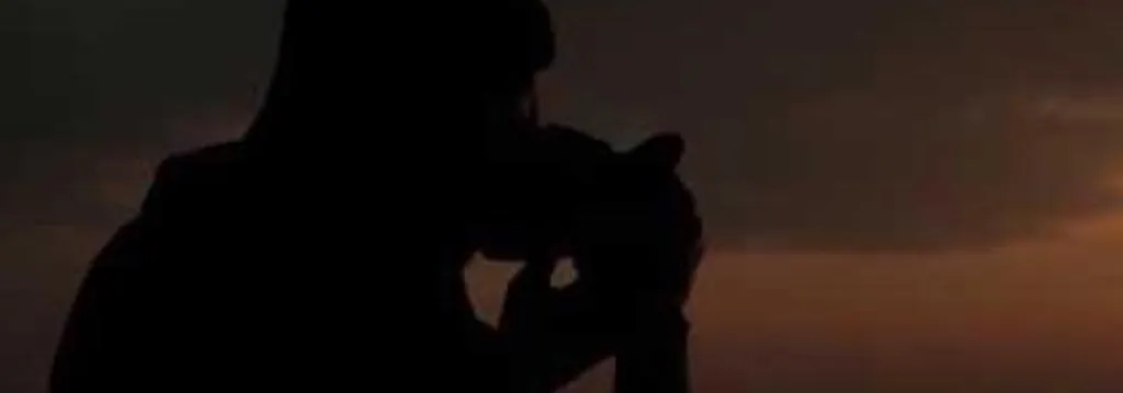 A silhouette lifting a camera against an orange dusk sky
